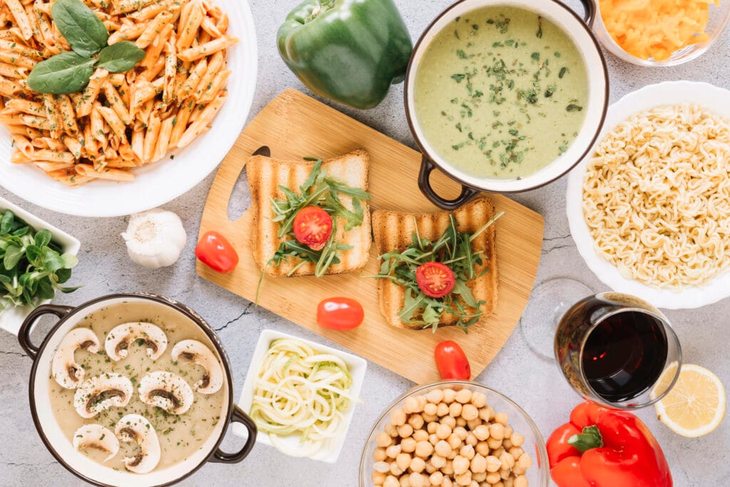 tavola imbandita di alimenti di vario tipo: zuppa, pasta, toast, ceci, vino, peperoni.